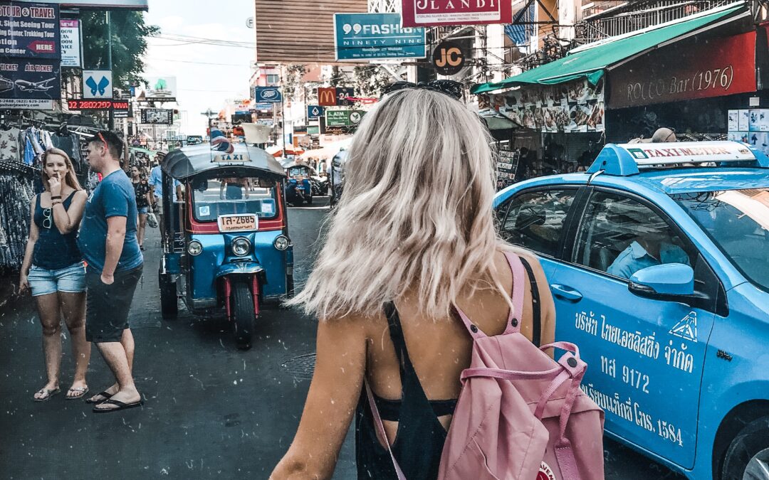 Ein Mädchen steht inmitten der Stadt Bangkoks, rundherum sind Geschäfte und Autos.