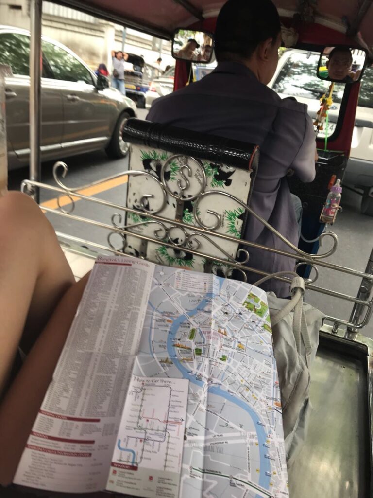 Neben einer Karte von Bangkok ist ein Fahrer eines Tut Tuns zu erkennen. 
