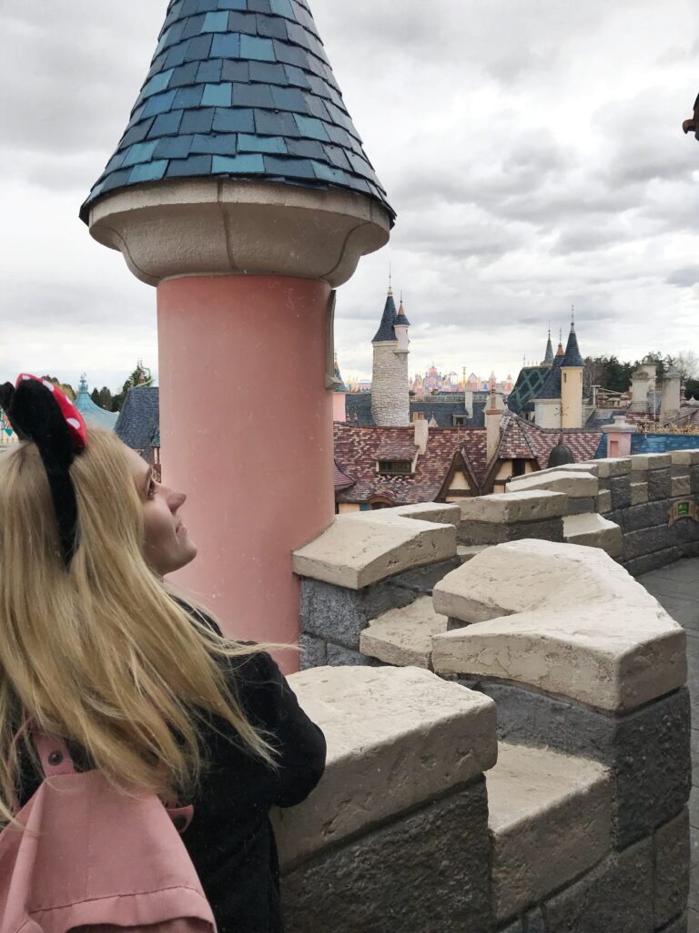 Ein Mädchen steht auf dem Dach vom Disney Schloss, neben ihr sind Türme. 