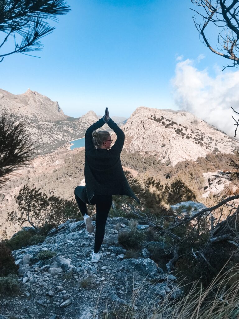 Ein Mädchen steht auf einem Berg und macht eine Yoga Pose.