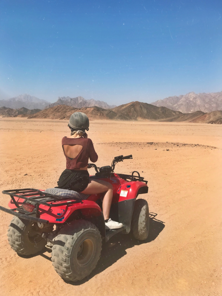 Ein Mädchen sitzt auf einem Quad, im Hintergrund ist die Wüste und Sand zu erkennen.